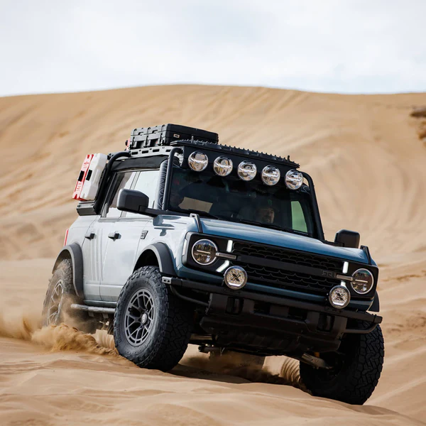 Off-road SUV navigating sandy dunes, equipped with roof lights and rugged tires, ideal for adventure travel.