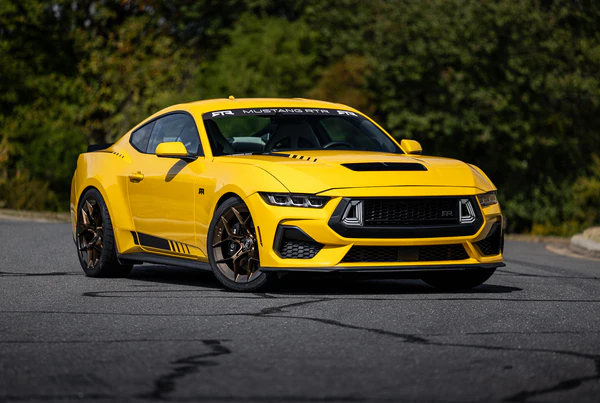 Yellow Ford Mustang GT on a road, showcasing sleek design and sporty features under sunlight.