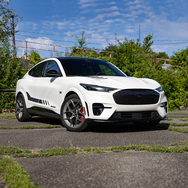 A sleek blue sports car in motion, showcasing its aerodynamic design and sporty features on a tree-lined road. The image captures the vehicle’s aggressive stance and distinctive wheels, emphasizing speed and performance.