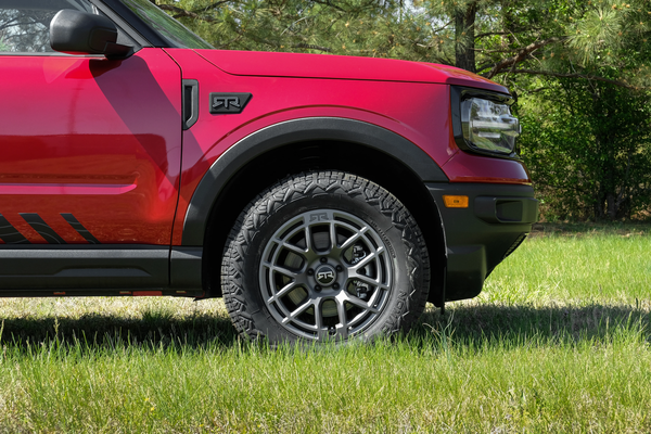 Red SUV with customized RTR wheels parked on grass, surrounded by lush greenery.