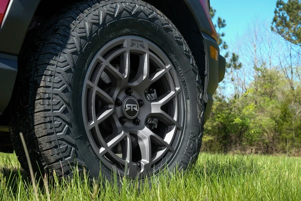 Off-road tire on a vehicle with rugged alloy rims, parked on grass in a natural setting.