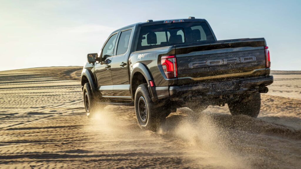 Ford Raptor driving through desert sand dunes, showcasing off-road capability and power.
